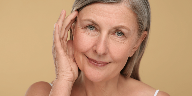 Donna matura con capelli grigi e pelle curata, tocca delicatamente il viso, simbolo di benessere e medicina anti-aging a Milano.