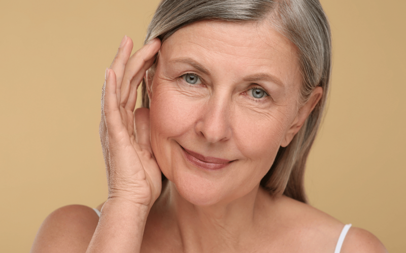 Donna matura con capelli grigi e pelle curata, tocca delicatamente il viso, simbolo di benessere e medicina anti-aging a Milano.